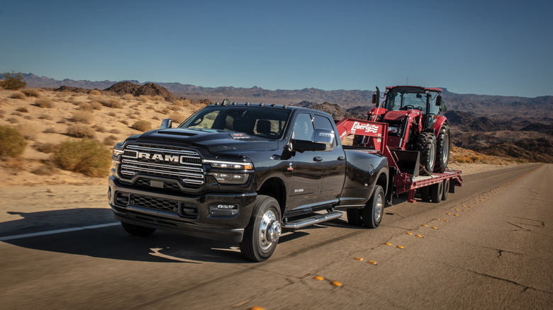 Black 2025 Ram 3500 Heavy Duty Laramie Edition pickup seen from front left towing a front end loader on a trailer