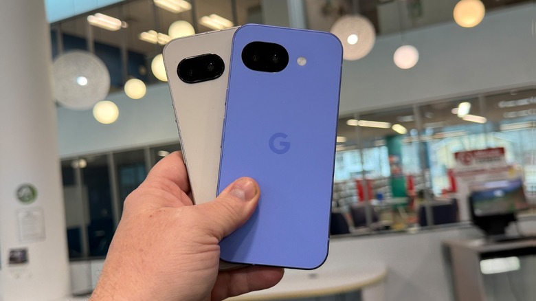 Hand holding up blue and gray Pixel 10a phones in an office environment