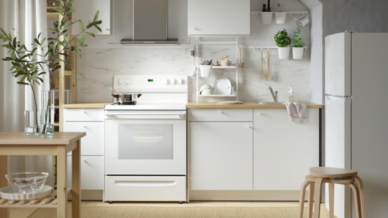 A simple kitchen with white Ikea flat-front cabinets, butcher block countertops, and a white freestanding electric range and a white refrigerator.