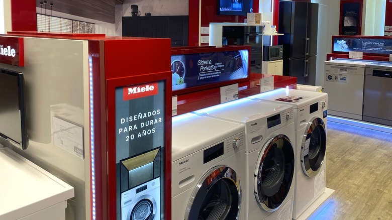 A Miele showroom display in a Spanish-speaking market featuring a row of front-load washing machines and other appliances at the background.