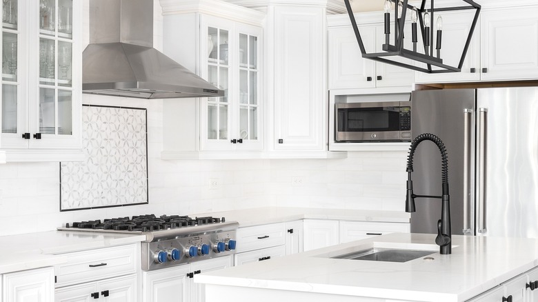 A bright all-white kitchen containing a glass-front upper cabinets, with a Thermador professional-grade gas range under a stainless steel hood.