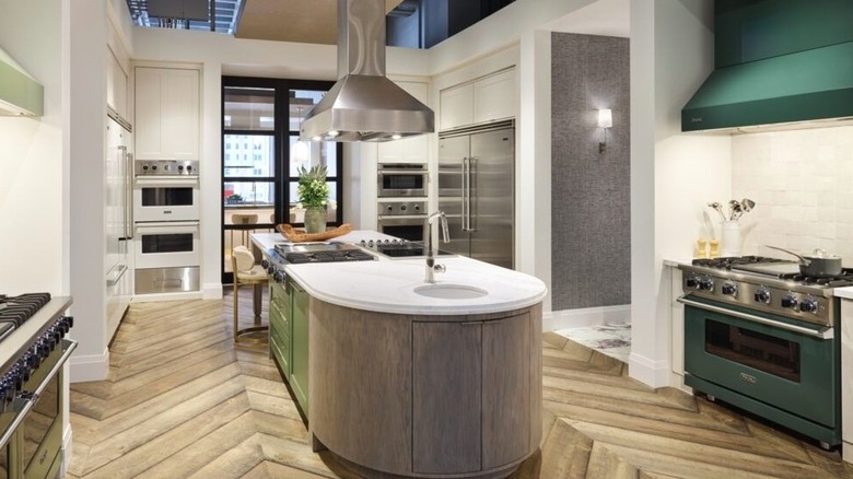 A high-end Viking kitchen showroom displaying a green range and a matching hood, stainless steel wall ovens, and refrigerators.