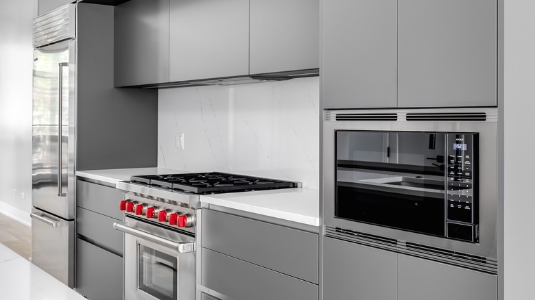 A gray kitchen with flat-panel cabinetry and a white marble backsplash featuring a Wolf gas range and a Wolf built-in microwave drawer.