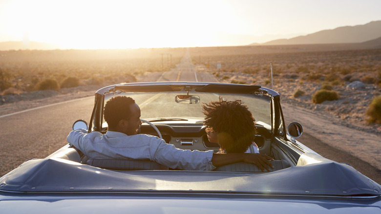 A couple on a road trip driving toward the sunset.