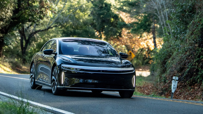 A black Lucid sedan traveling along a road, lined with vegetation.