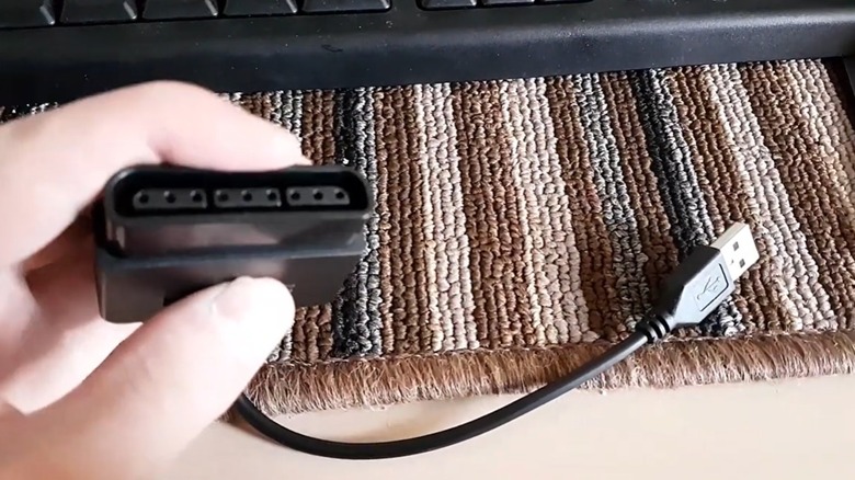 A person's hand holding an adapter meant to convert PlayStation 2 controllers to a USB connection