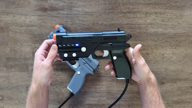 A person's hands holding a light gun in front of a table with another light gun lying on it