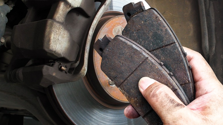 hand holding brake pads with rotor in background