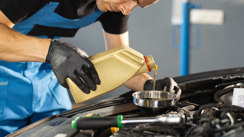 mechanic pouring motor oil into a funnel above an engine