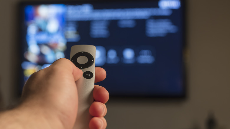 A hand holding up an Apple remote to a TV