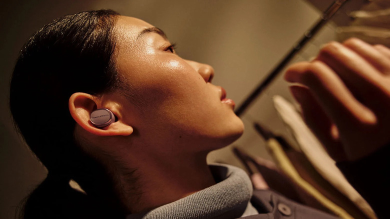 A person wearing the Bowers & Wilkins Pi8 wireless earbuds near a rack of clothes