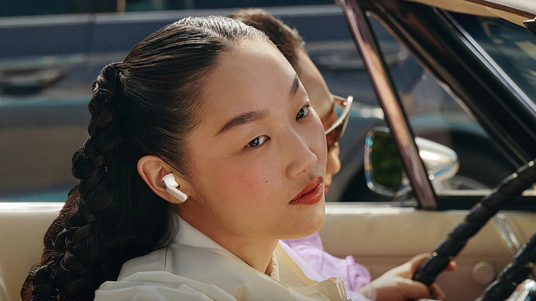 A person wearing the Samsung Galaxy Buds4 Pro earbuds in a car, sitting next to a person holding the wheel and wearing shades