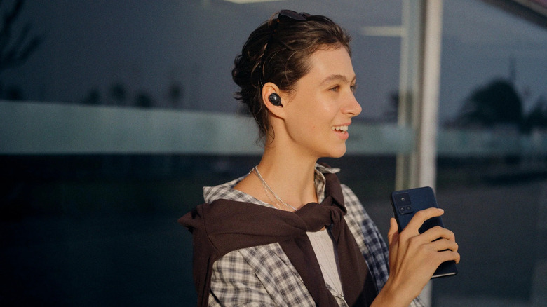 A person wearing the Sennheiser Momentum True Wireless 5 earbuds while holding a phone