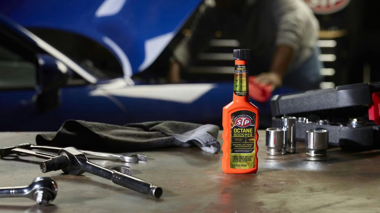 STP octane booster on an automotive workshop table, mechanic and car in background