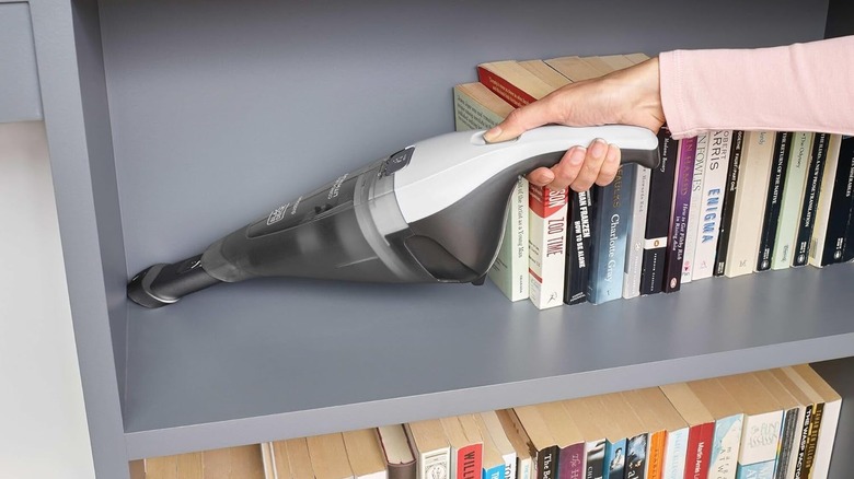 A woman is shown using a Dustbuster to remove dust from a bookshelf.