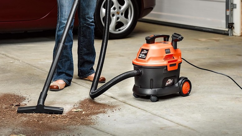 A woman is pictured using a Armor All AA255W Wet/Dry Utility Vac to vacuum dirt from a driveway.