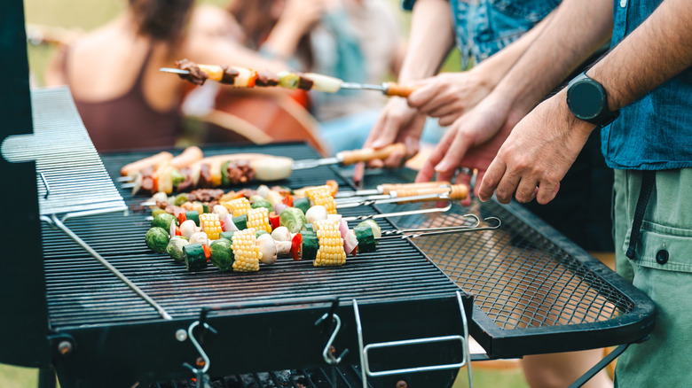 man grilling multiple skewers on large grill