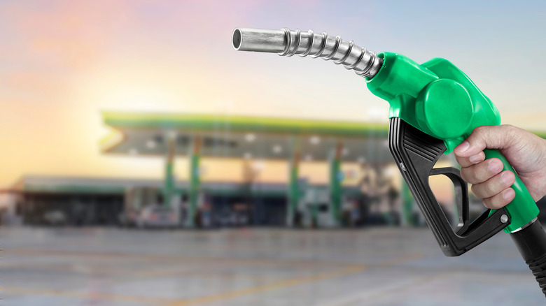 Green fuel nozzle with gas station in background