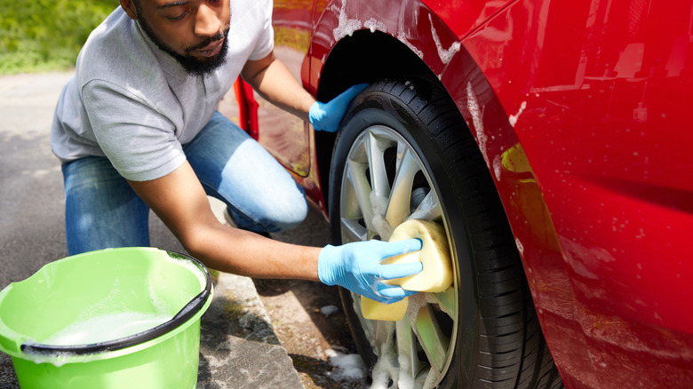 Man washing a red car with a bucket and sponge