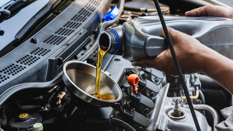 Mechanic pours oil into engine through a funnel