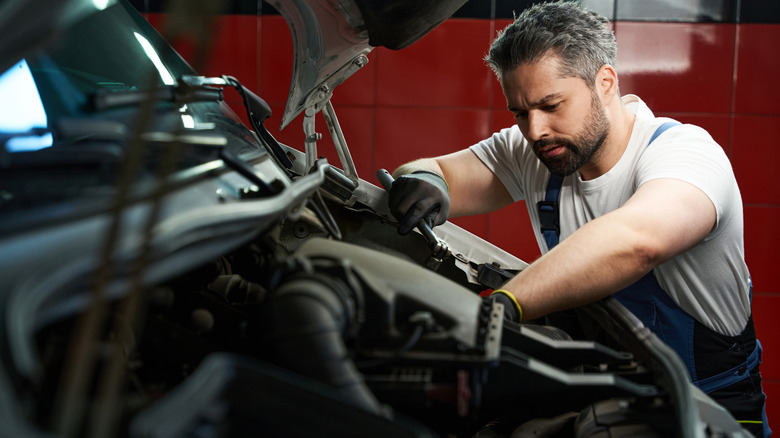 Mechanic works under the hood of a car in a repair shop