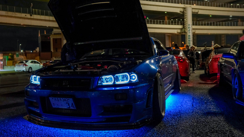 A car with blue underglow lighting and blue headlamps on display at a car show