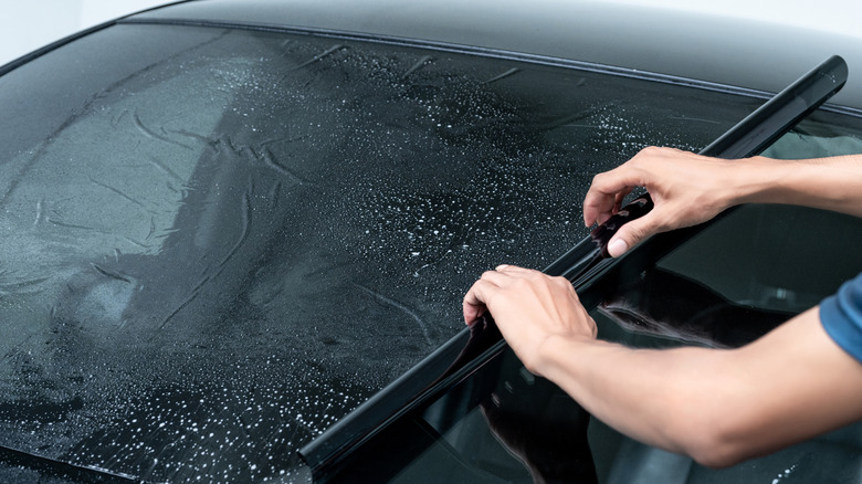A person applying tint film on a car windshield