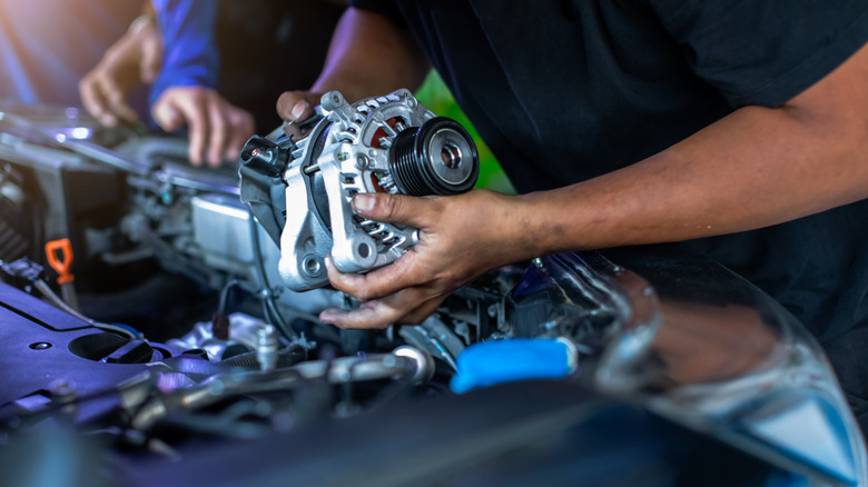 Mechanic holding a car's alternator with the engine open