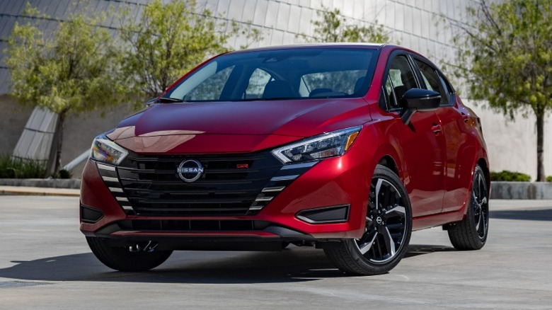 Red Nissan Versa parked with a concrete structure in the background