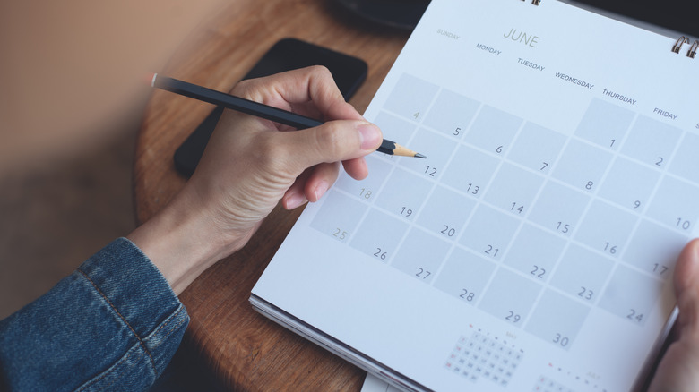 Person holding pencil over calendar