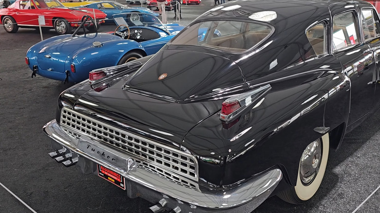 Rear-side view of a 1949 Tucker 48 in bright blue, parked beside a rustic wooden barn