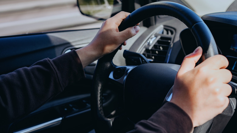 a young man with two hands on a car steering wheel