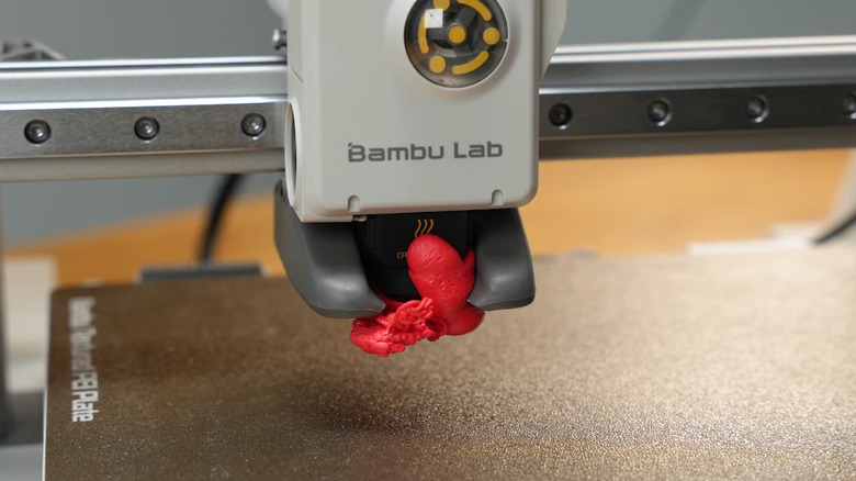 A 3D printer with red filament blob attached.