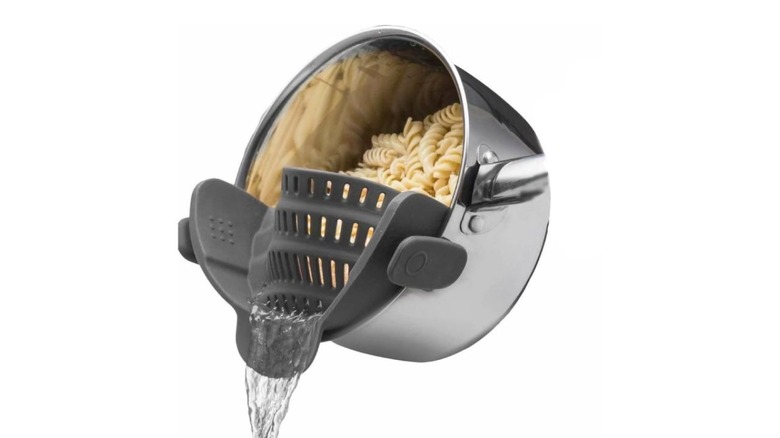 The Kitchen Gizmo Snap N' Strain silicone clip-on water strainer on a white background, used to take water out of a pot with pasta.