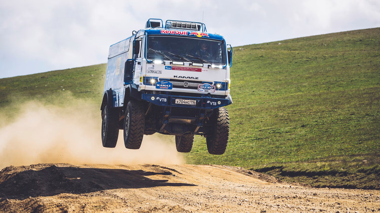 A Kamaz truck suspended in the air while racing on a dusty path.
