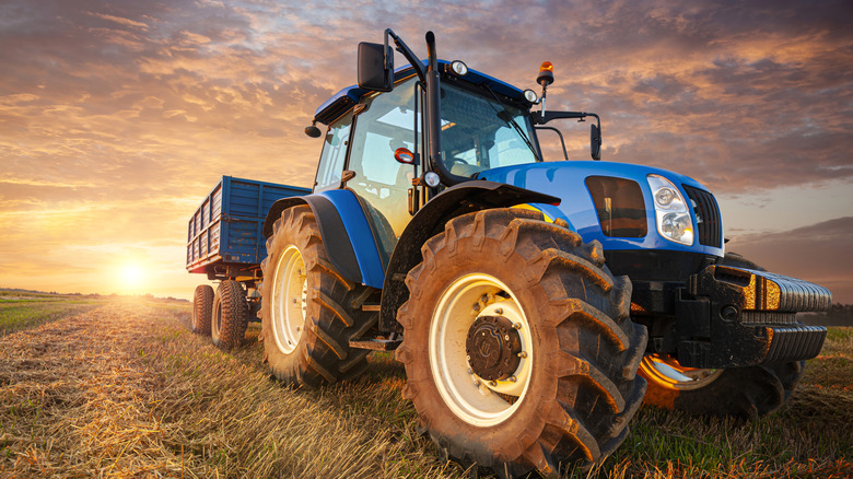 A blue tractor pulling cargo with the sun going down behind it.