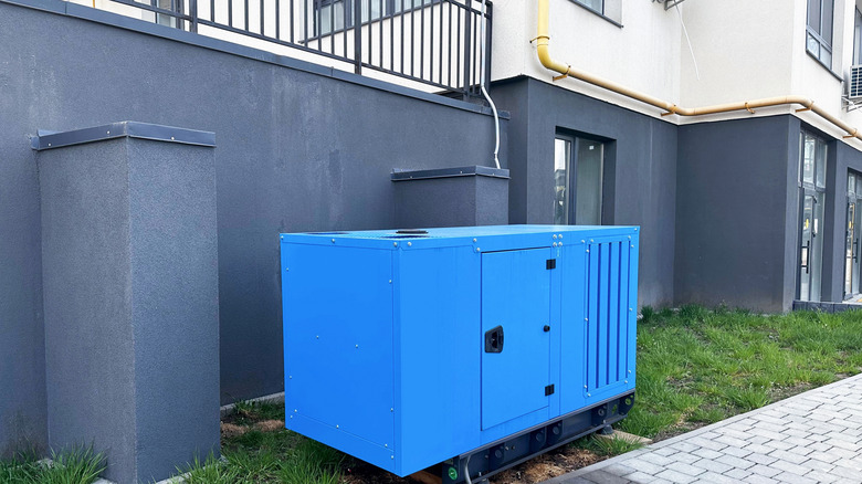 A blue diesel generator stationed on the lawn outside a house.