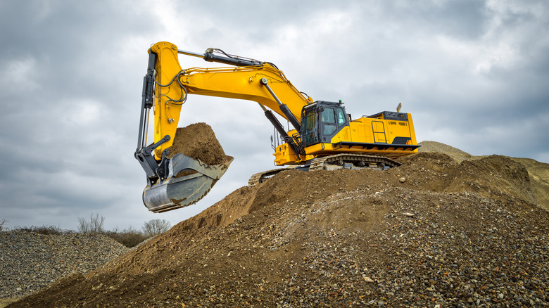 An excavator digging up the earth with a cloudy sky in the background