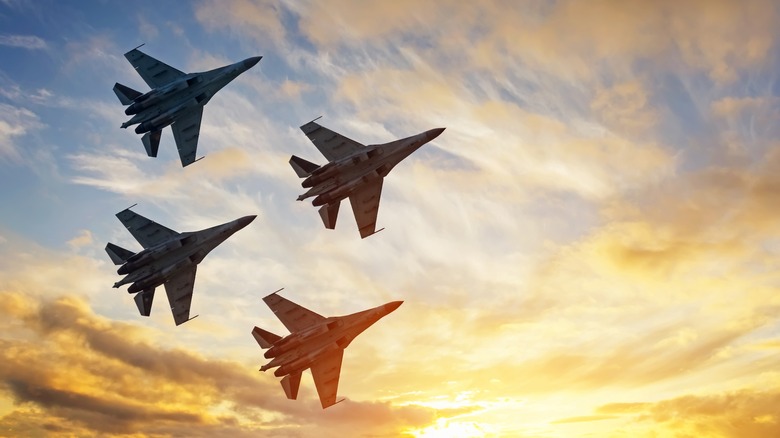 4 fighter jets flying in front of a sunset