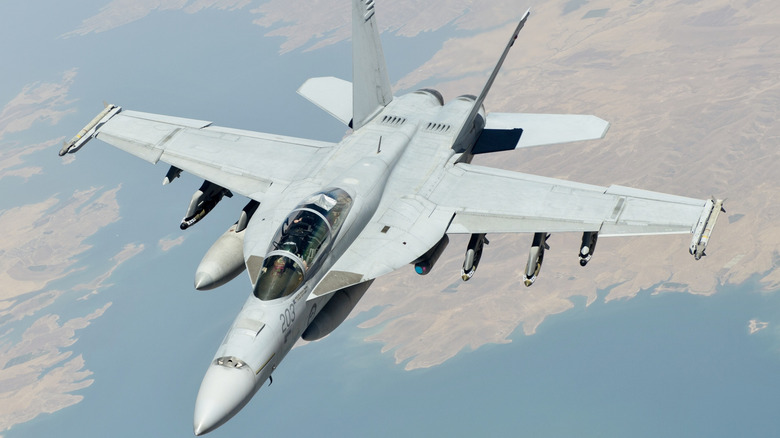 F/A-18F Super Hornet fighter jet seen from above and left on patrol above a desert coastline