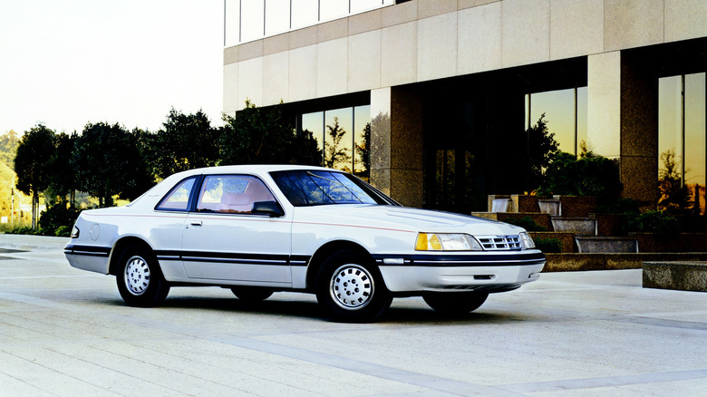 White 1987 Ford Thunderbird coupe seen from front right parked in front of office building at twilight