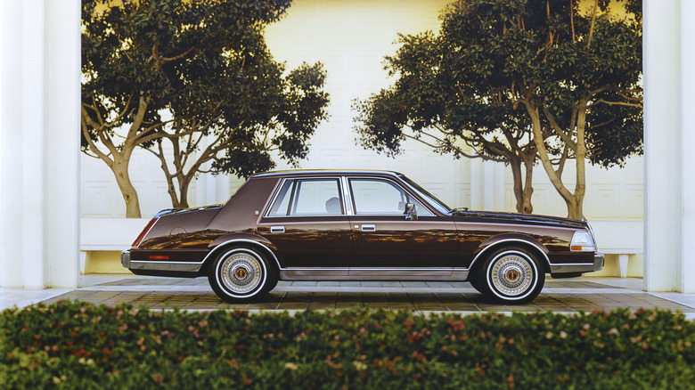 Brown 1985 Lincoln Continental sedan seen from left parked near lush landscaping