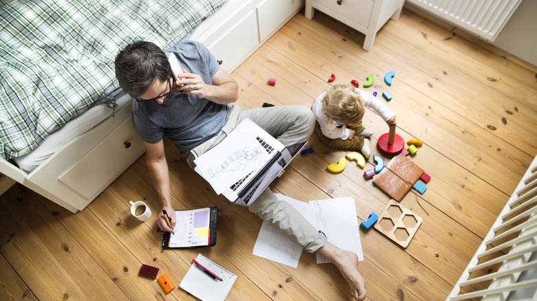 Father sitting with child on floor while working