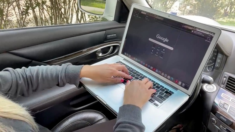 A person working on a laptop mounted on a car's steering wheel