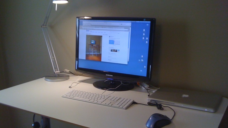 A bare home office with a computer monitor, a laptop, and a standard desk lamp atop a standing desk