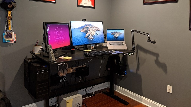 An example of a home office setup, with no fewer than three screens, a microphone, and a fancy desk