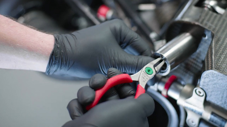 Mechanic using a pair of Facom pliers to adjust parts of a race car.
