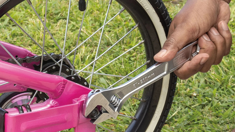 A Black+Decker wrench adjust the nut on a bike wheel.