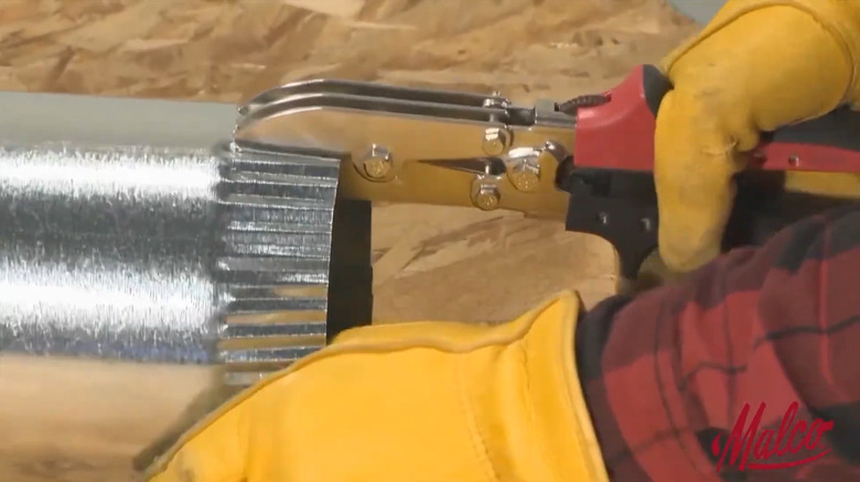 A worker using a pair of Malco Tools' Round Duct and Stove Pipe Crimping tool.