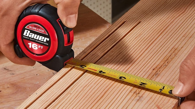 Person stretching a tape measure across a board